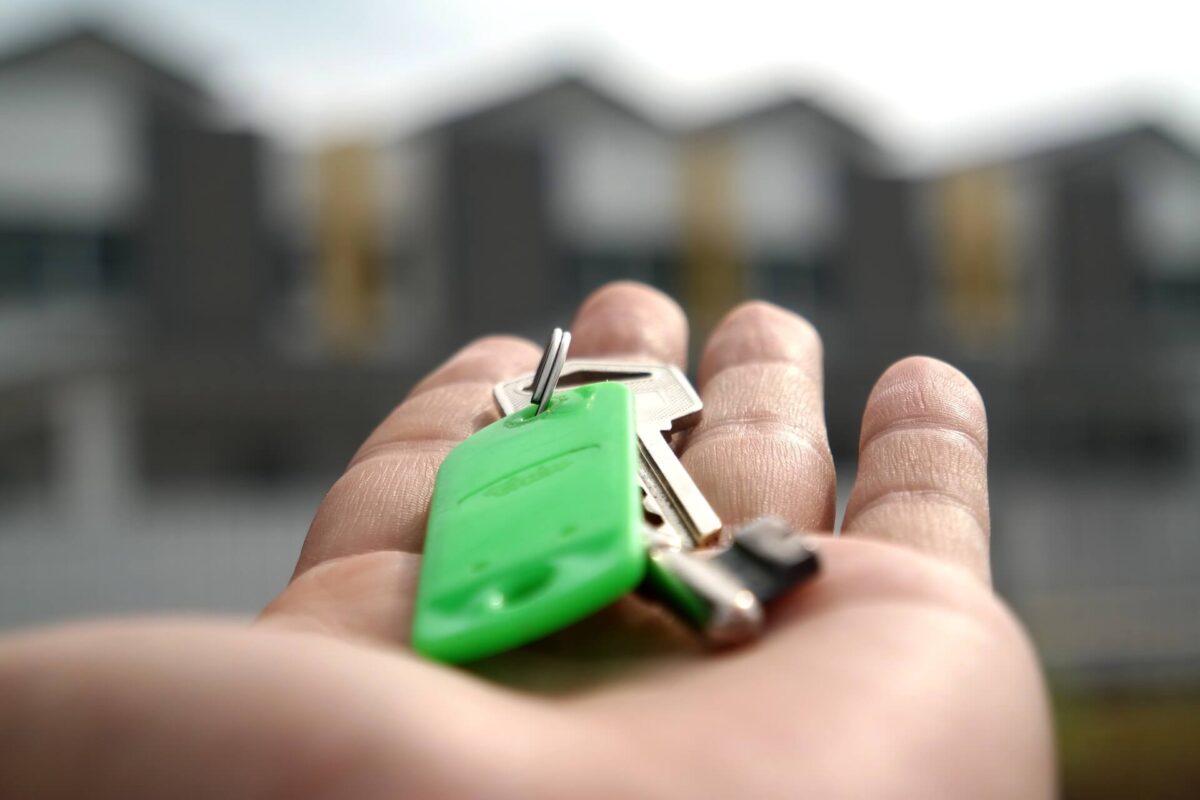 Close up of a hand holding house key with home in the background