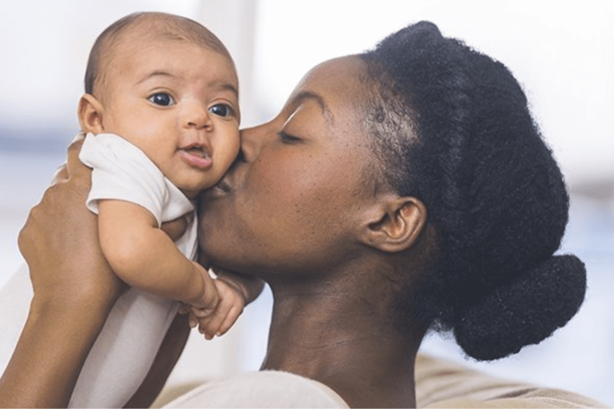 A young Black mother holds and kisses her baby