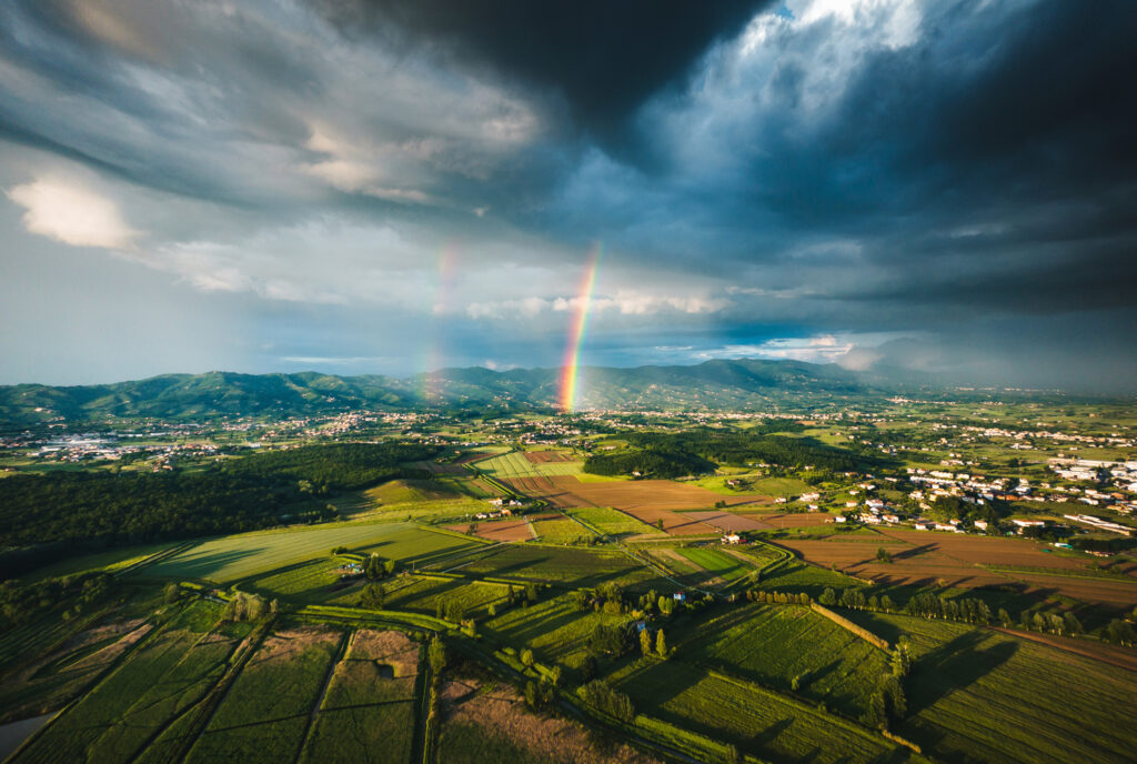 A rainbow breaks through a clearing in storm clouds over a rural landscape